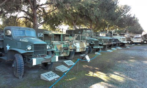 1994 Ford Bronco - A collection of vintage military trucks are displayed in a row under trees, with some showing camouflage paint.