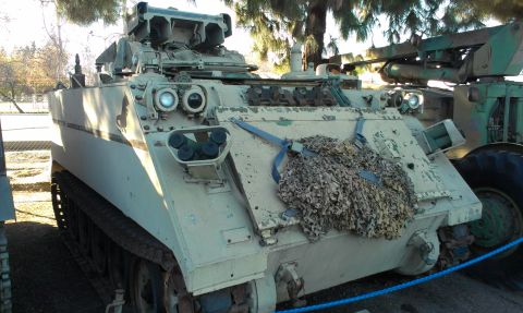 1994 Ford Bronco - A tan armored personnel carrier with a missile launcher is parked next to another military vehicle.