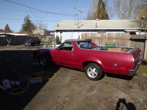 1978 Ford Ranchero - A red pickup truck with a bed is parked in a yard next to a house and fence.