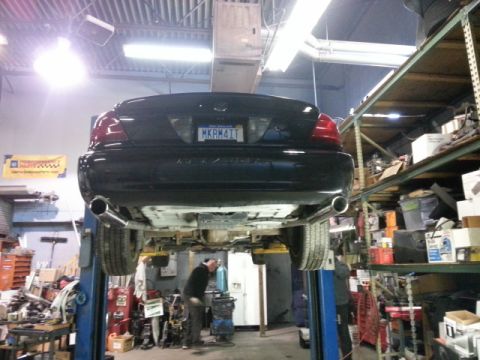 2004 Mercury Grand Marquis - A black sedan is raised on a hydraulic lift in a workshop, with its underside exposed for service.