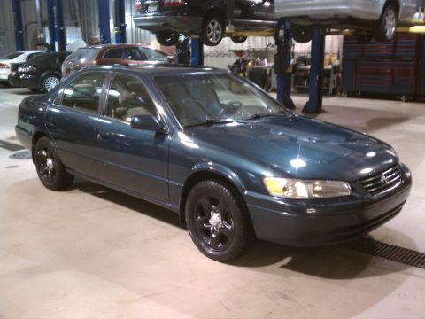 1998 Toyota Camry - Dark teal sedan with black wheels in a garage, with another car lifted above.