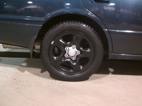 1998 Toyota Camry - Close-up of the rear wheel and fender area of a dark green sedan, showing a black rim and tire.
