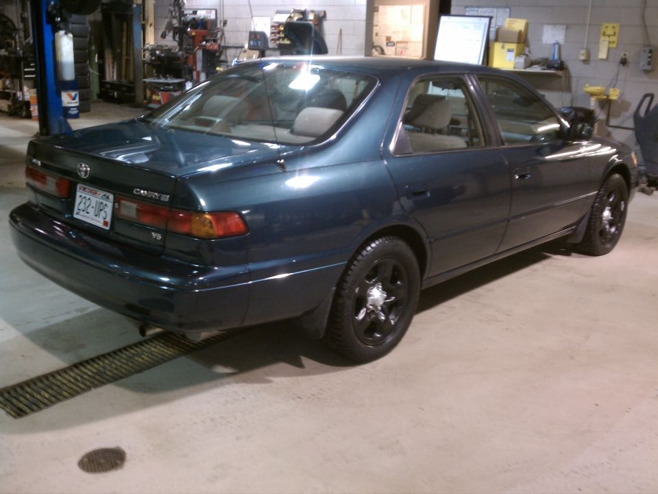Dark blue 1998 Toyota Camry sedan with black wheels, seen from the rear-left in a garage