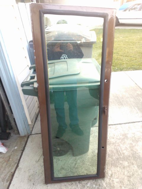 1968 Ford Bronco - A brown door window frame is shown, with reflections of a person and trash cans visible in the glass.