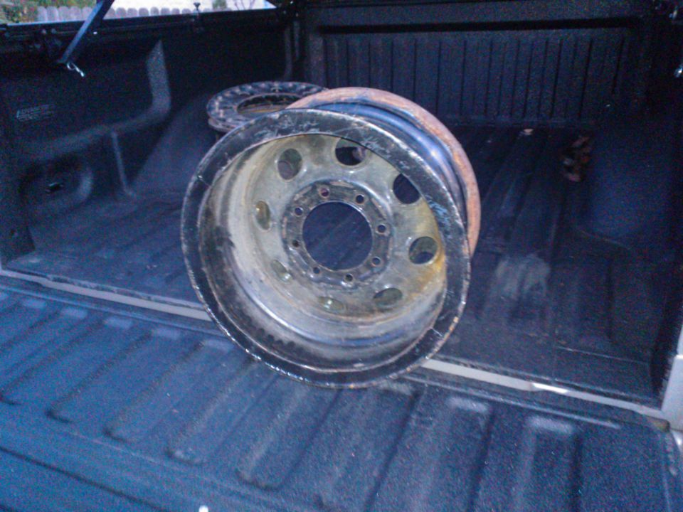 Two rusty wheels are in the bed of a pickup truck. One wheel is in the foreground, and another is behind it