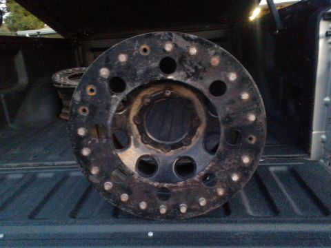 1968 Ford Bronco - A single black wheel with numerous bolt holes is shown in the back of a truck.