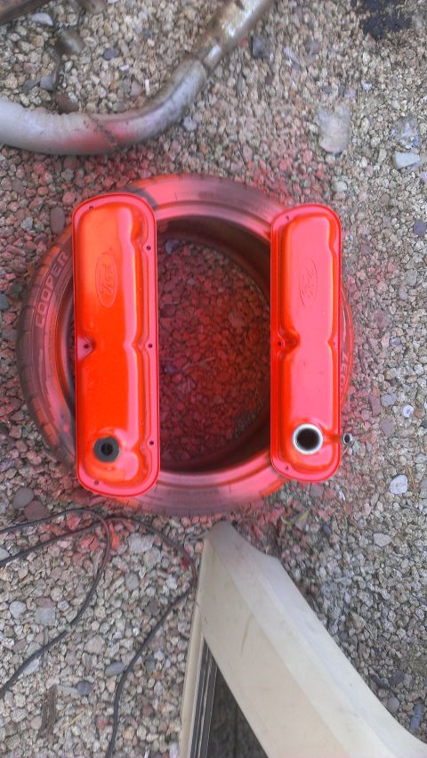 1990 Ford Bronco - Two orange Ford valve covers are placed on a tire, with gravel and an exhaust pipe visible in the background.
