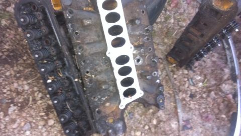 1990 Ford Bronco - Engine cylinder heads and intake manifold gasket are shown lying on the ground.