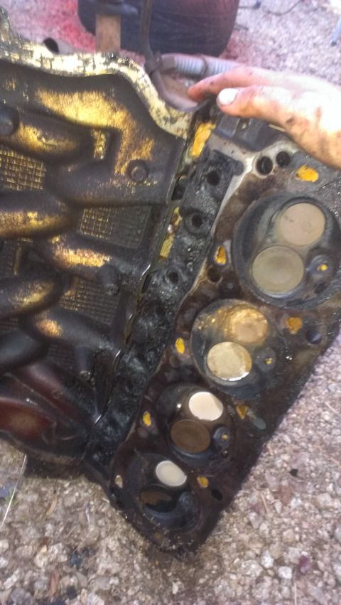1990 Ford Bronco - A heavily soiled engine cylinder head is held by a hand, showing multiple valves.