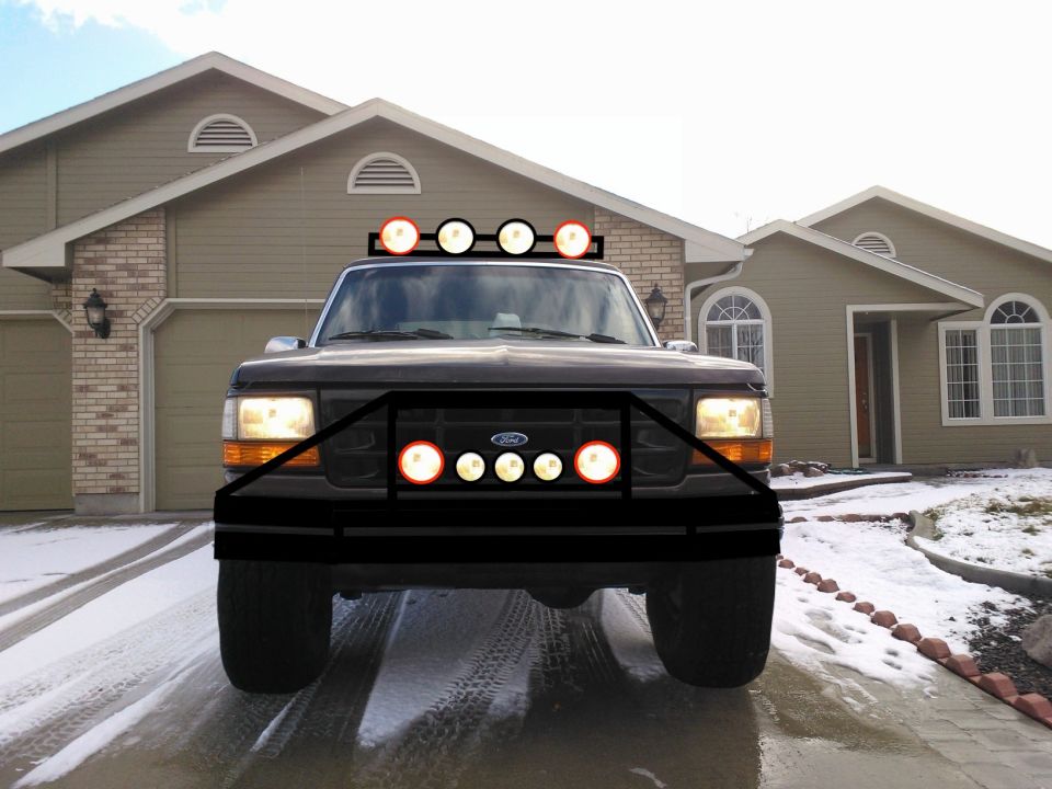 Front view of a dark-colored Ford truck with a large black aftermarket bumper and multiple lights mounted on the roof and bumper