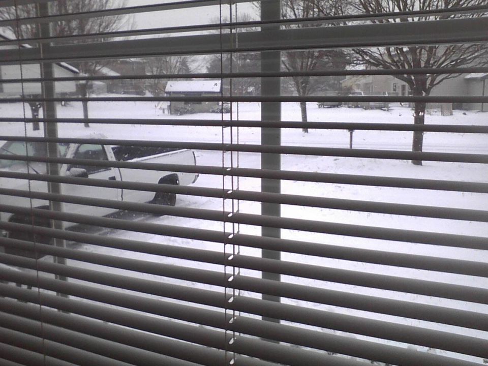 White pickup truck partially obscured by blinds, parked on a snow-covered street