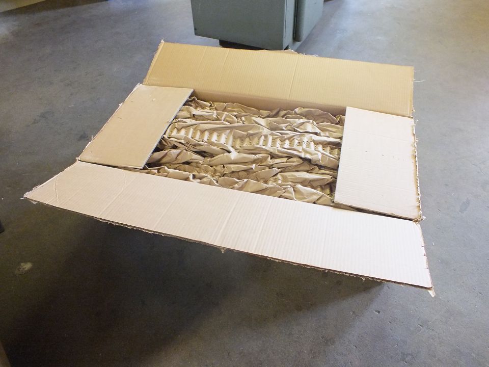 Open cardboard box with crumpled kraft paper packing and stainless pipe inside