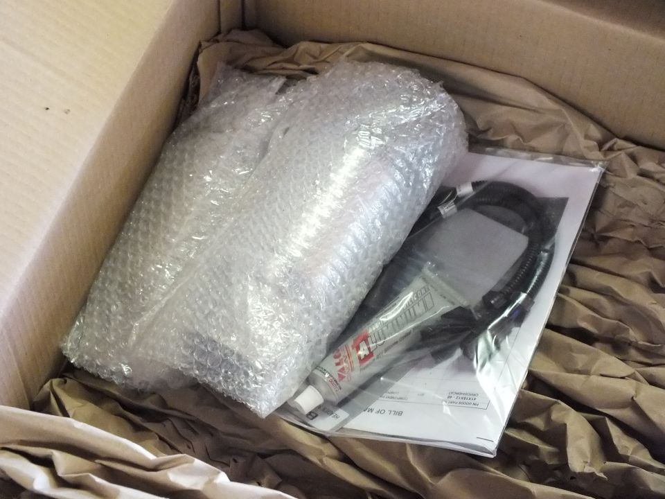 Bubble-wrapped exhaust parts beside O2 sensor extension and instruction sheet in box