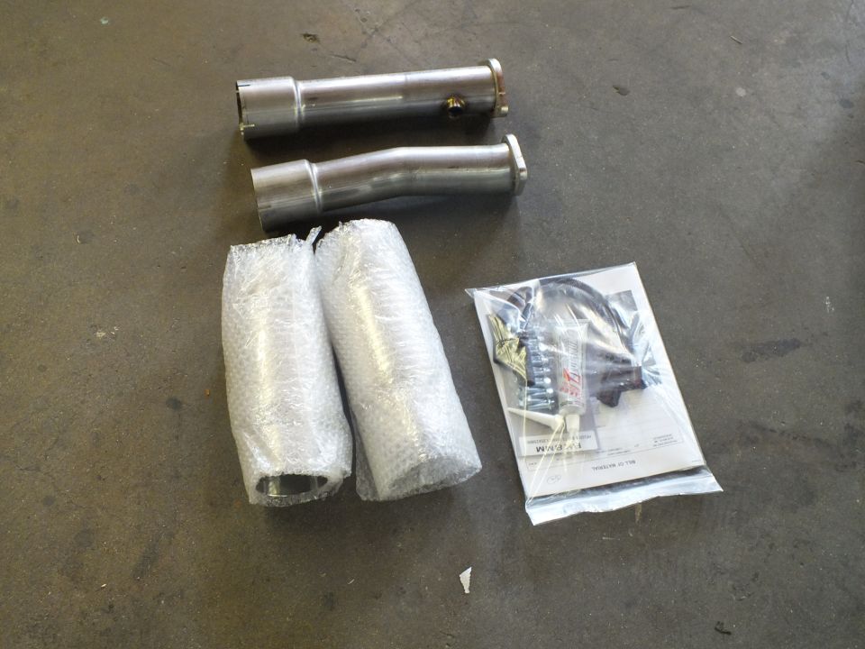 Stainless exhaust pipes, bubble-wrapped parts, and hardware bag laid out on floor