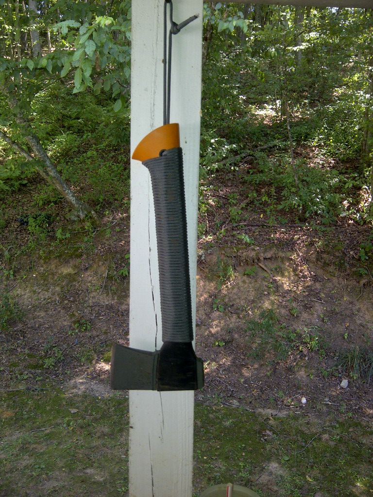 Axe with orange and black handle hanging on a white post