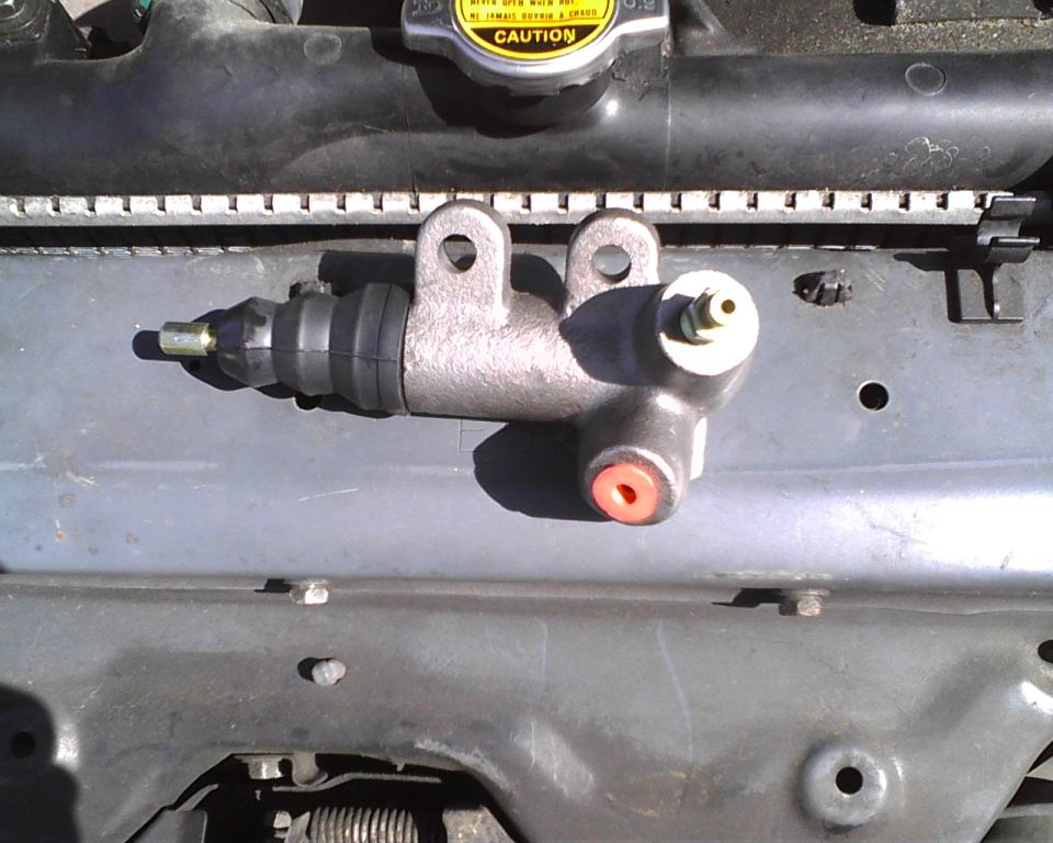 Clutch master cylinder with rubber boot and banjo fitting, resting on car engine components