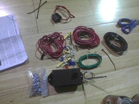2003 Ford Crown Victoria - Various electrical wiring components are laid out on a wooden floor, including spools of wire, connectors, and a fuse holder.
