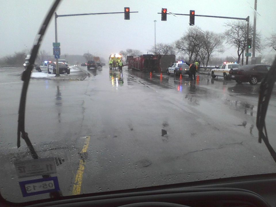 Accident scene with police cars, overturned truck, and emergency personnel on a wet road