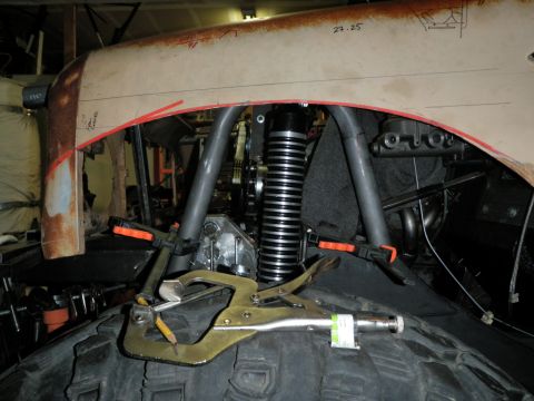 1961 International Scout 800 - Work in progress on a vehicle's fender and suspension system, with clamps securing a large tire.