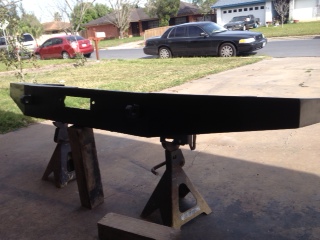1990 Ford Bronco - A custom bumper is shown on jack stands in a driveway, with residential buildings and vehicles in the background.