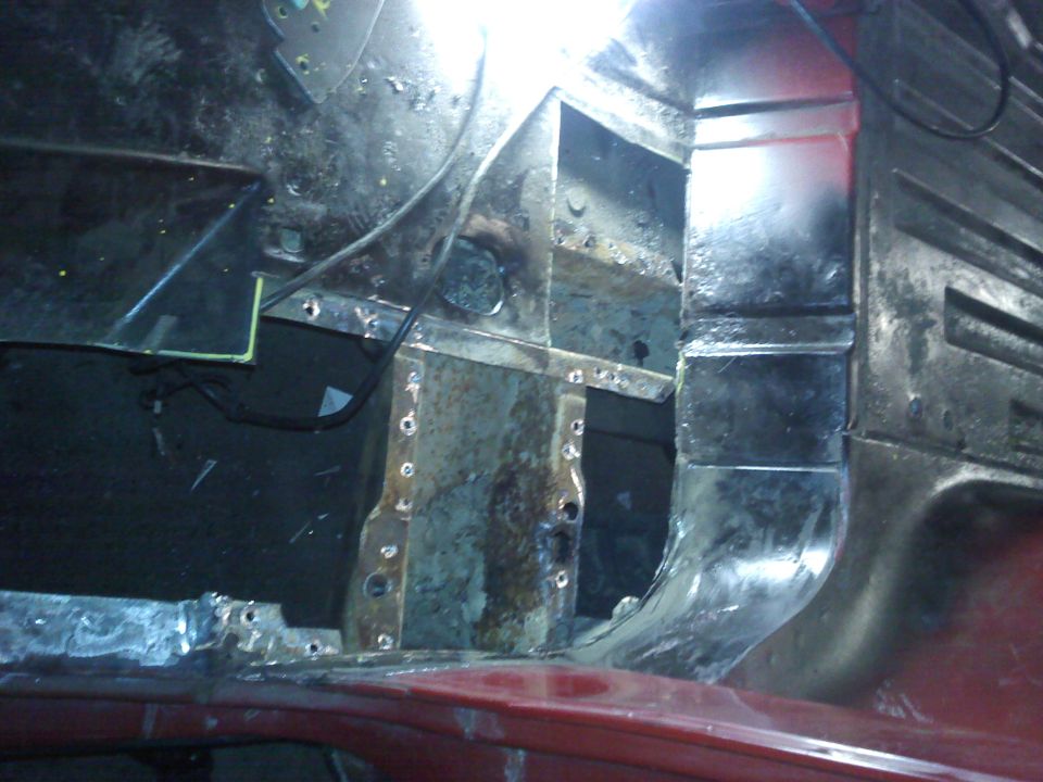 Rusted metal interior of a red vehicle, showing structural damage and repair work