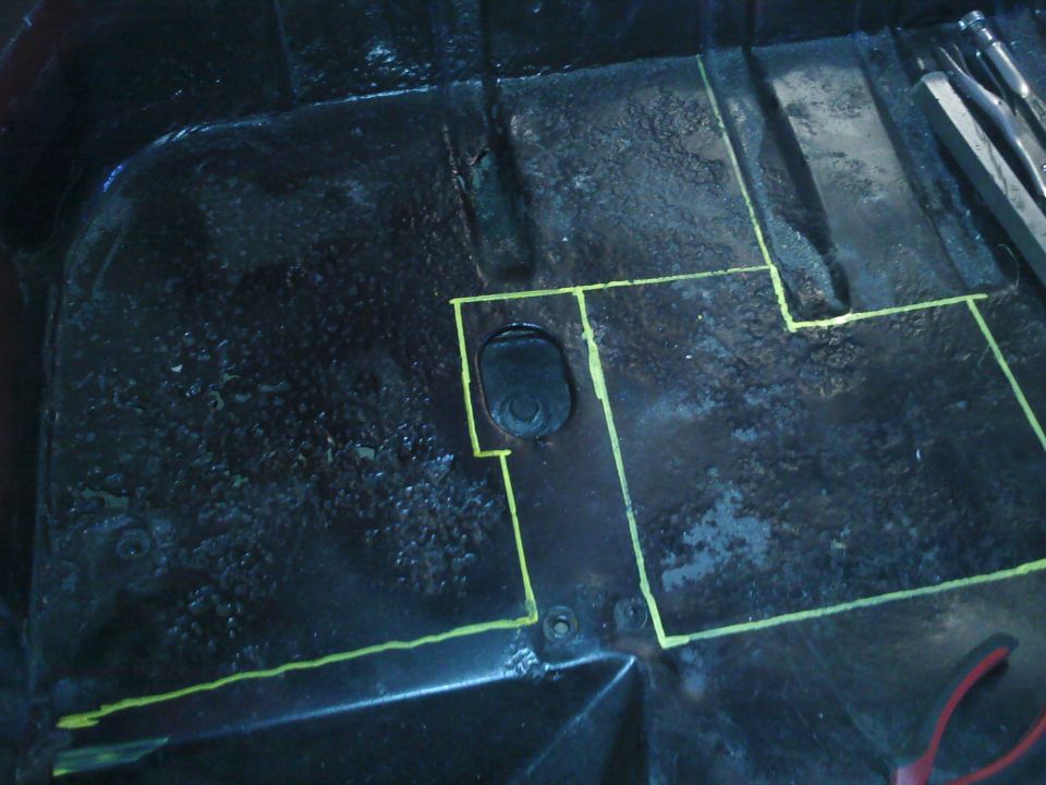 Vehicle floor pan with yellow tape marking cut lines, a black grommet, and some tools in the upper right
