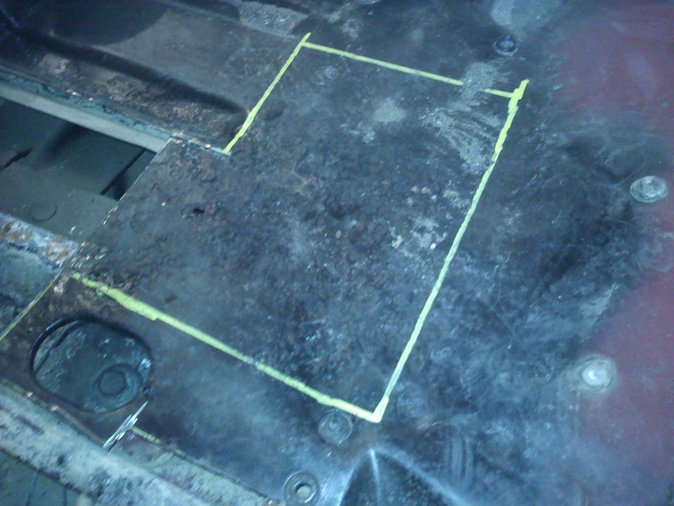 Metal floor panel with yellow chalk lines indicating a cut area. Some rust and bolts are visible