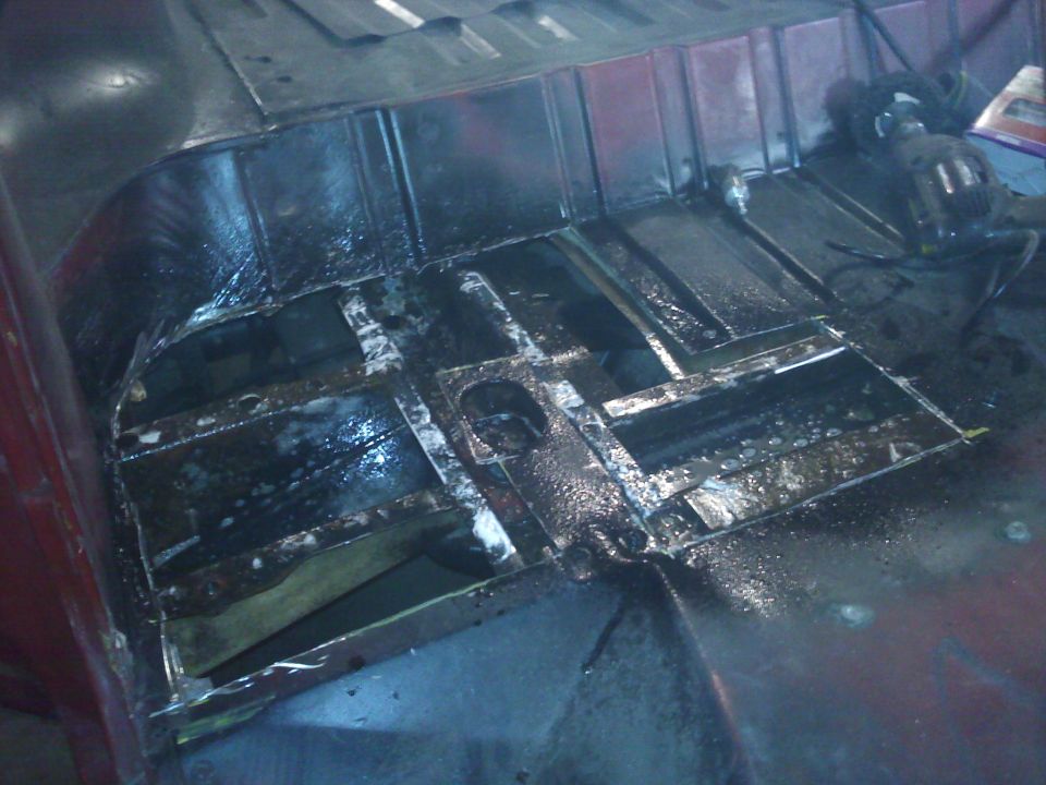 Interior floor of a vehicle undergoing repair, showing exposed metal and some rustproofing