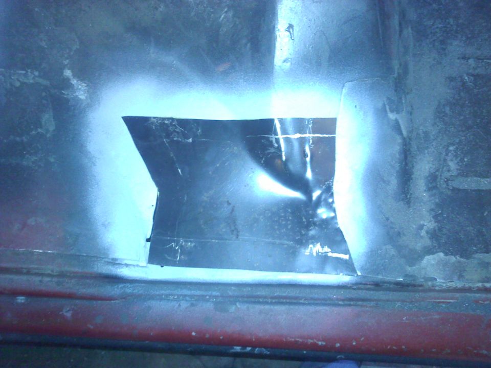 Metal patch covers hole in red car body panel, spray paint around edges