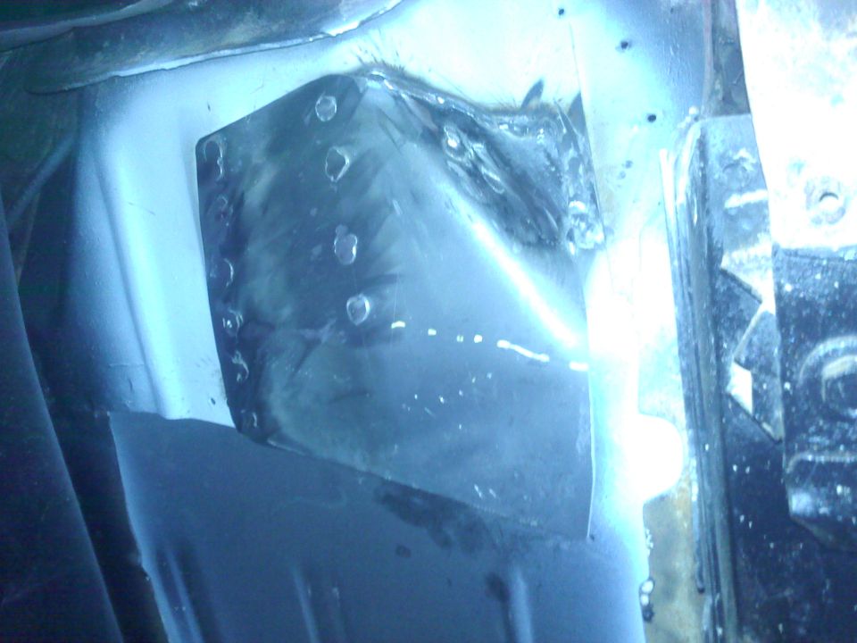 Welded metal patch on vehicle frame, showing rivets and a bright light source