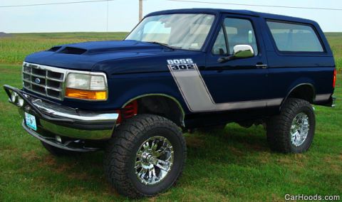 1994 Ford Bronco - A dark blue Ford Bronco full-size SUV shown from the front three-quarter angle, lifted on chrome wheels with large off-road tires, featurin…