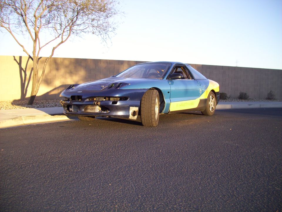 1993 Ford Probe with blue, yellow, and dark blue paint sections, missing front bumper cover