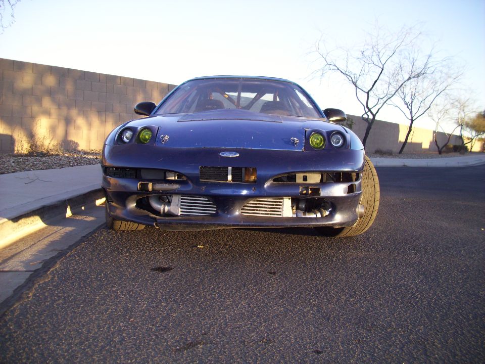 Front view of a blue sports car with exposed intercoolers and yellow fog lights