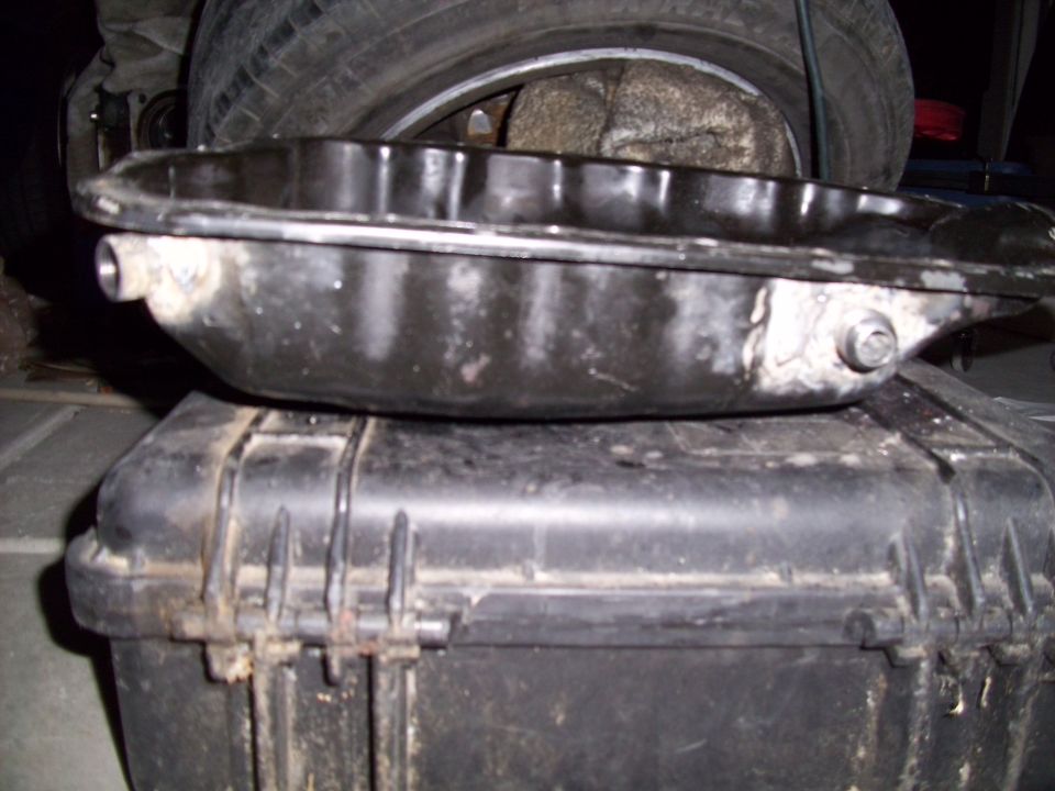 black oil pan resting on a black plastic case, with a tire in the background