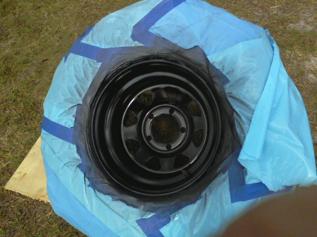 Black steel wheel covered with blue tarp and tape for painting