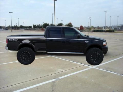 1992 Ford Bronco - Side view of a black Ford F-150 pickup truck with 4x4 badging and large aftermarket wheels.