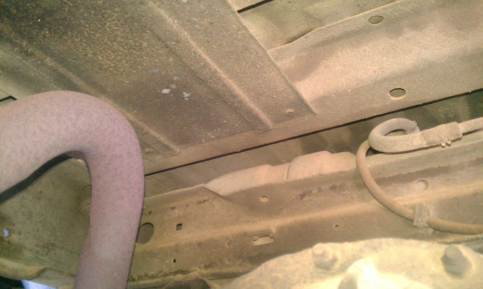 Underside view of a vehicle showing an exhaust pipe and a fuel line. No specific year or model is identifiable