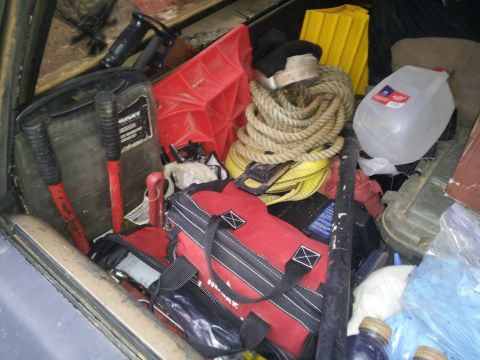 1986 Ford Bronco - The interior of a vehicle is filled with various tools and equipment, including a red toolbox and a large coil of rope.
