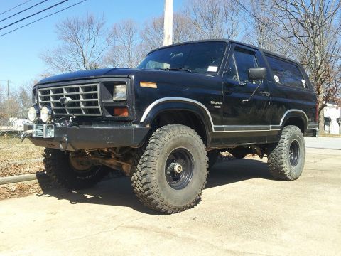 1986 Ford Bronco - This black Ford Bronco, likely from the early 1980s, is equipped with large off-road tires and a modified front bumper.