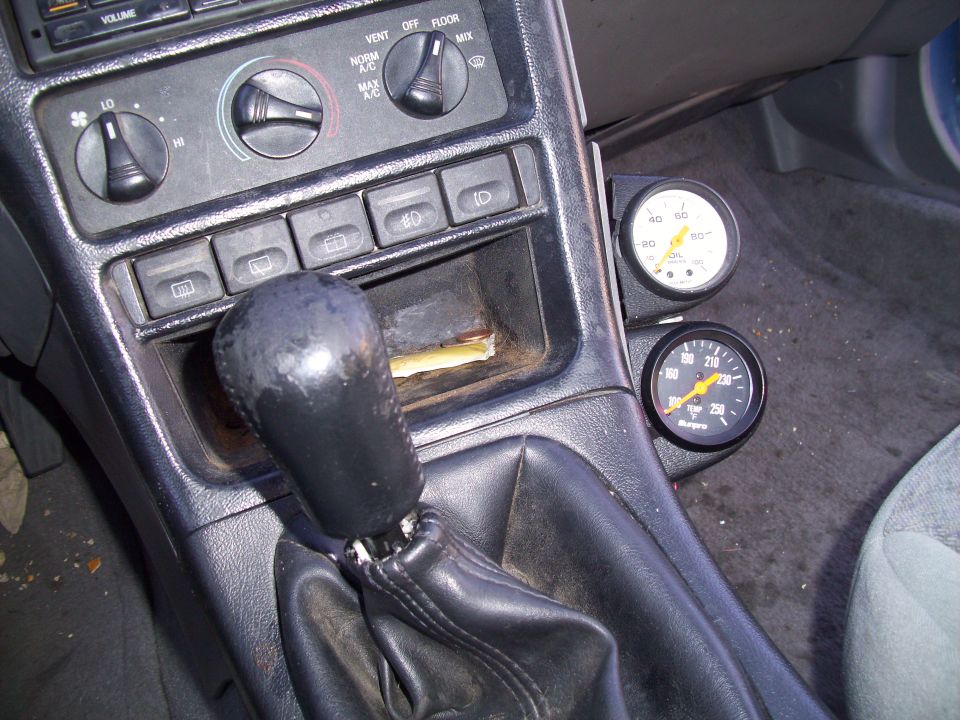 Car interior center console with gear shifter, climate controls, and two aftermarket gauges mounted to the right