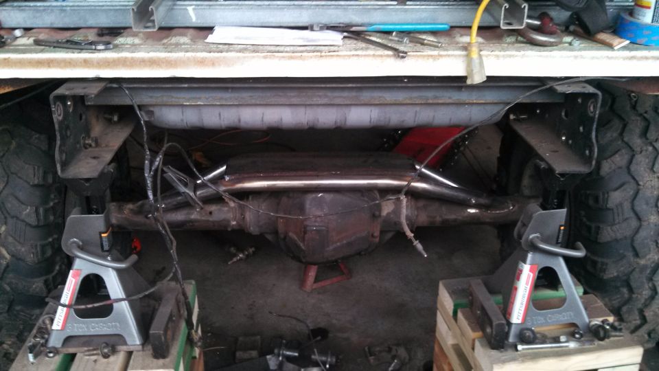 Truck rear axle assembly on jack stands, showing differential, exhaust, and tires