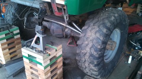 1967 Ford F-250 - Vehicle's rear axle and large tire are supported by jack stands and wooden blocks in a garage setting.