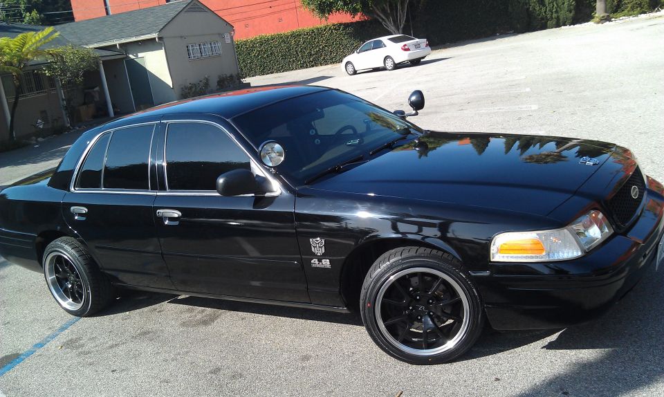Black Ford Crown Victoria sedan with blacked-out wheels parked in lot, front quarter view