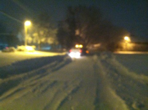 1989 Ford Bronco - A car's taillights glow brightly as it navigates a snowy road under streetlights.