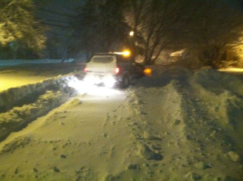1989 Ford Bronco - A white SUV navigates a snow-covered road at night, its taillights and an orange roof light illuminating the scene.