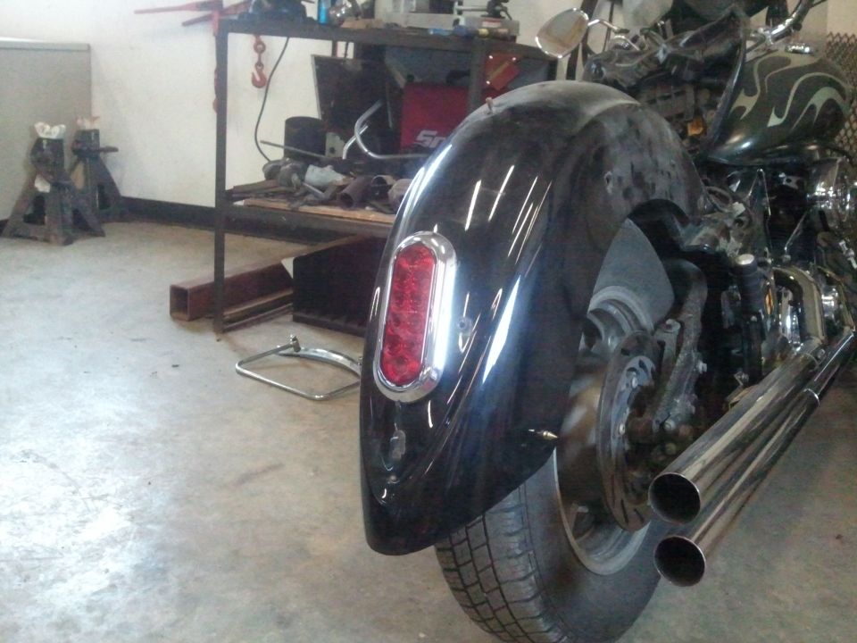 Black motorcycle fender with a red taillight and dual chrome exhaust pipes