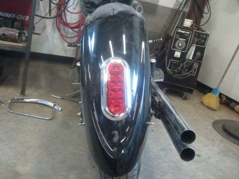 1995 Ford F-150 - Rear view of a motorcycle's fender, showing its taillight and exhaust pipes in a workshop setting.