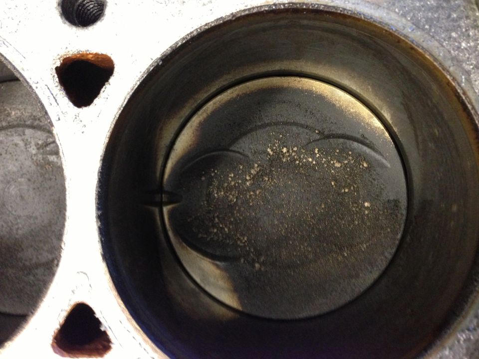 Engine cylinder with piston showing carbon buildup and debris