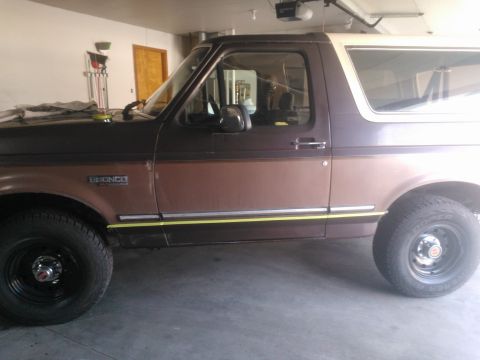 1992 Ford Bronco - Side view of a brown and white 1992 Ford Bronco with yellow trim, parked indoors.