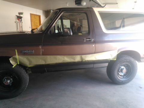 1992 Ford Bronco - A 1992 Ford Bronco is shown in a garage with masking tape applied to the lower body panels, likely in preparation for painting.